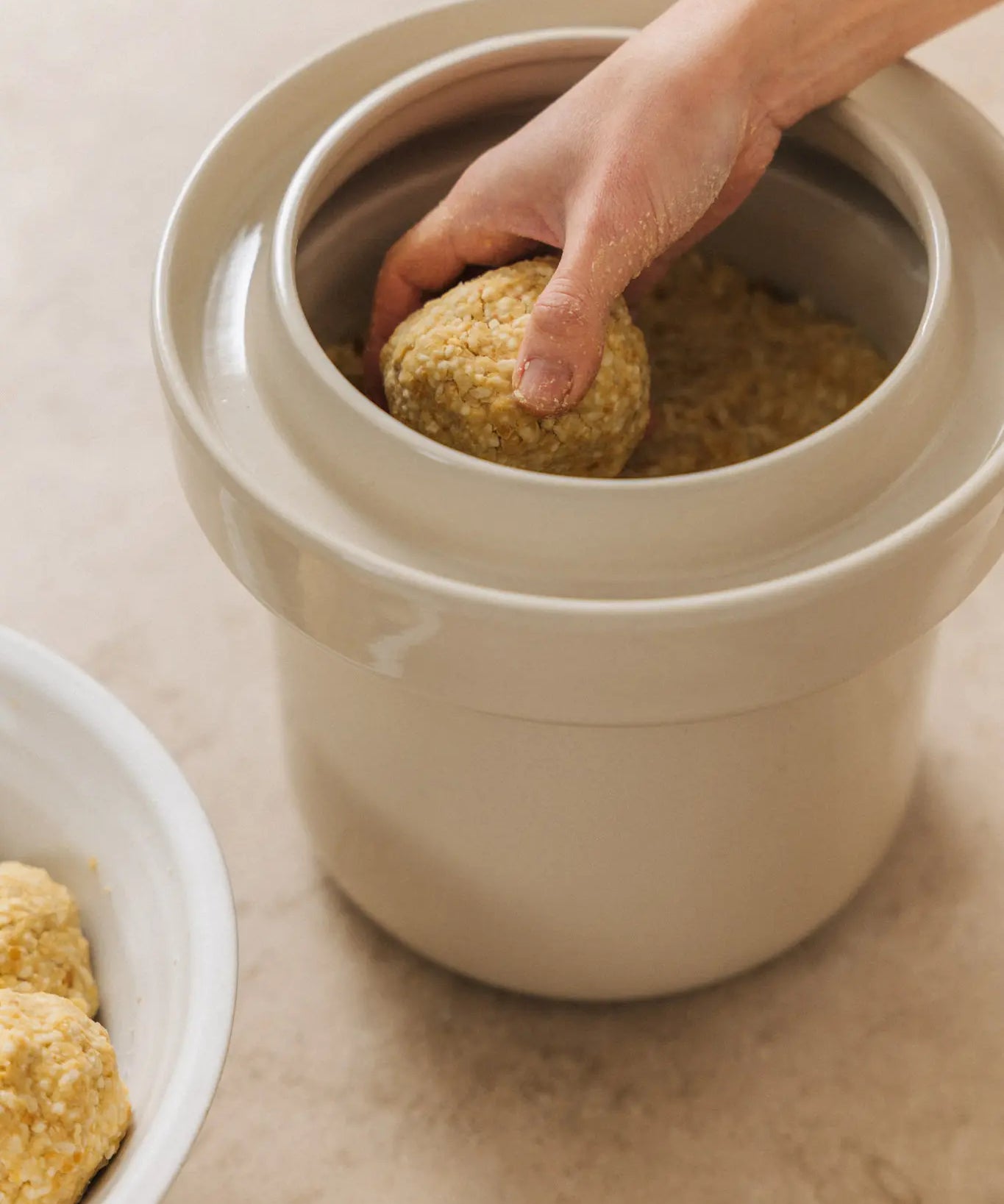 traditionelle herstellung von kichererbsen-miso: miso-paste wird von hand in einen steinguttopf zur fermentation gefüllt. der prozess markiert den start der 3 bis 12 monate langen reifezeit für lebendiges umami.