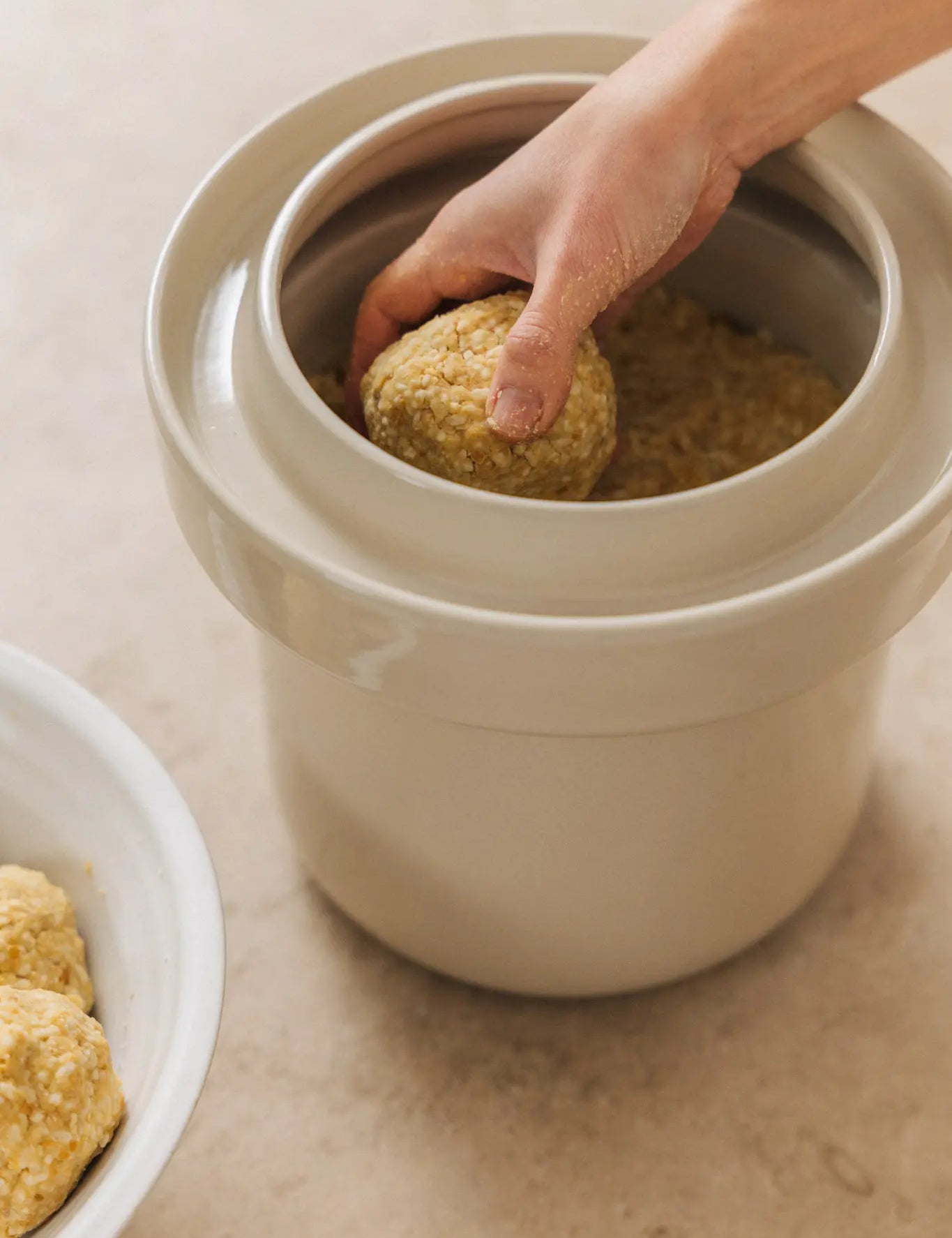 traditionelle herstellung von kichererbsen-miso: miso-paste wird von hand in einen steinguttopf zur fermentation gefüllt. der prozess markiert den start der 3 bis 12 monate langen reifezeit für lebendiges umami.